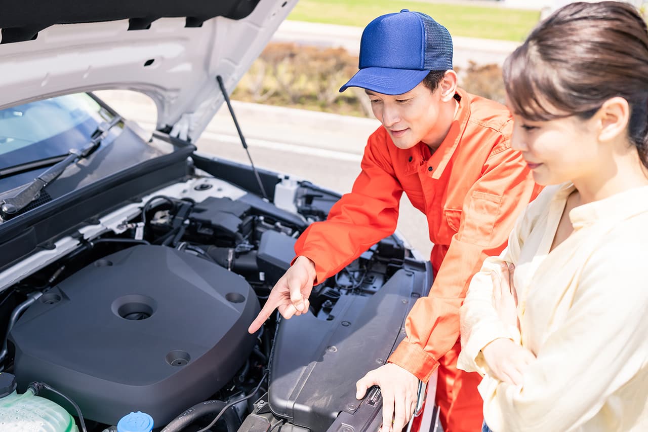 車のフロント部分を女性に説明している整備士